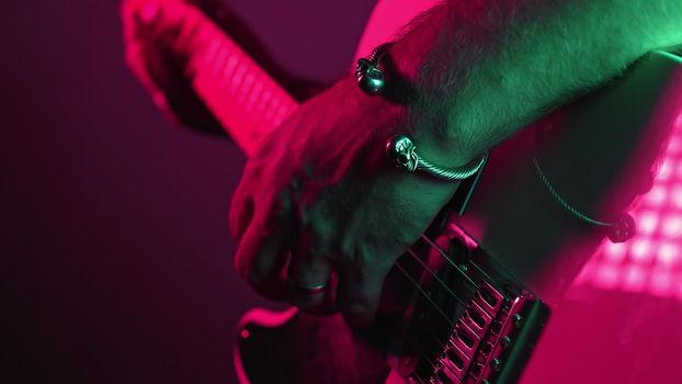 Rock guitarist man on smoky stage masterfully playing electrical guitar. Musician plays music during concert under neon colorful light. High quality photo