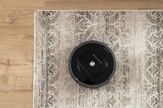 Top view of a black robotic vacuum cleaner that cleans the carpet.