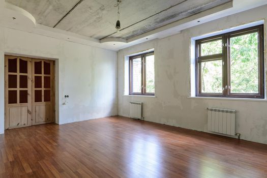 Interior of an empty room during renovation, view of a wall with windows and a wall with a door a