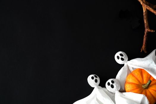 Three white ghosts hold orange pumpkin on black background, halloween symbols. Flat lay, postcard, copy space