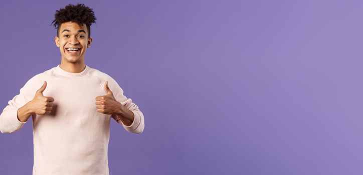 Portrait of upbeat, happy smiling man left pleased after using company service, studying at online language school, show thumbs-up and look camera, recommending, stand purple background.