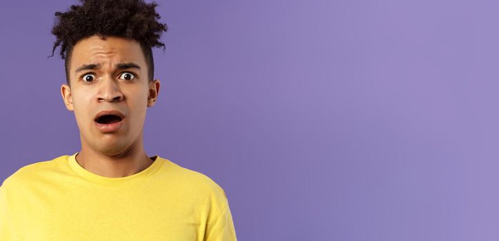 Close-up portrait of shocked, alarmed young man gasping, open mouth scared and frightened, staring camera concerned, facing troublesome shocking news, purple background. Copy space