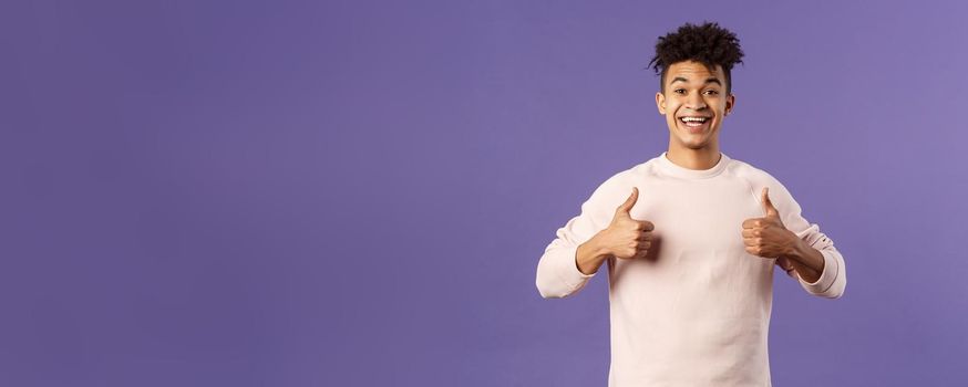 Portrait of upbeat, happy smiling man left pleased after using company service, studying at online language school, show thumbs-up and look camera, recommending, stand purple background.