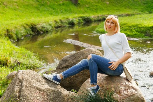Beautifyl young woman in casual style sitting on stone in park