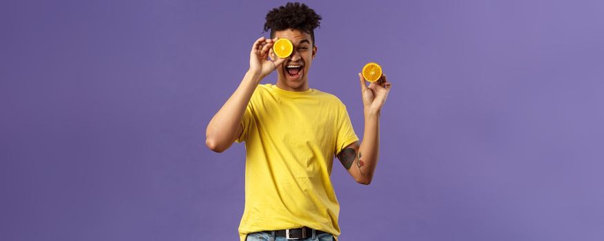 Holidays, vitamins and vacation concept. Portrait of carefree, upbeat good-looking man having fun, look playful laughing, likes eating fruits healthy food, holding pieces of oranges.