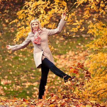 young woman playing with autumn leaves in park