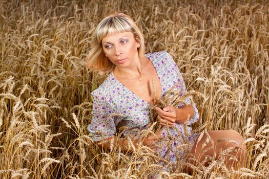 beautiful woman sitting on wheat field at sunset