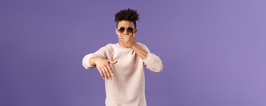 Waist-up portrait of cool and sassy, young carefree guy with dreads and sunglasses, cover mouth to beatbox, waving hand in rhythm music, singing rap or attend hip-hop party, purple background.