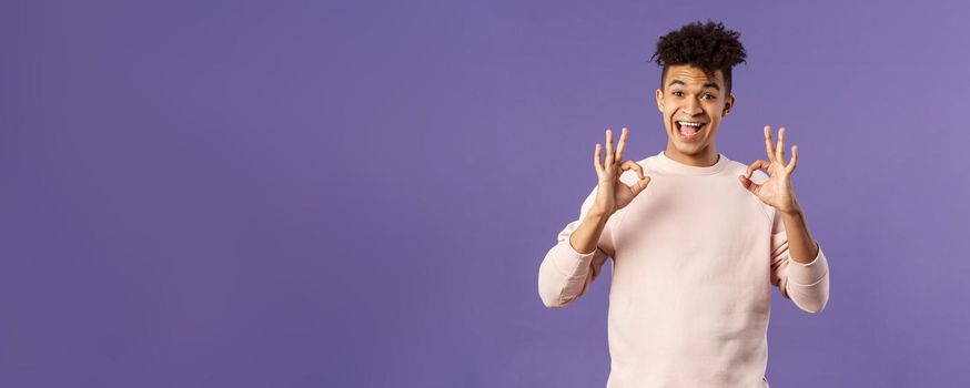 Portrait of satisfied young male student recommend online business school or education courses, give excellent feedback, show okay gesture as approve or like something really good.