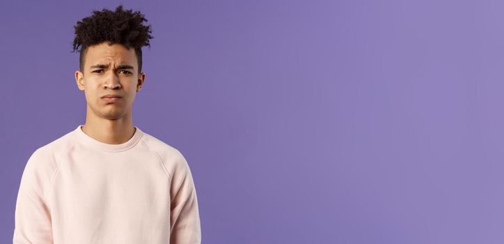 Close-up portrait of skeptical and gloomy, disappointed hispanic young man frowning upset, feel uneasy about bad idea, grimacing with disapproval, standing unhappy purple background.