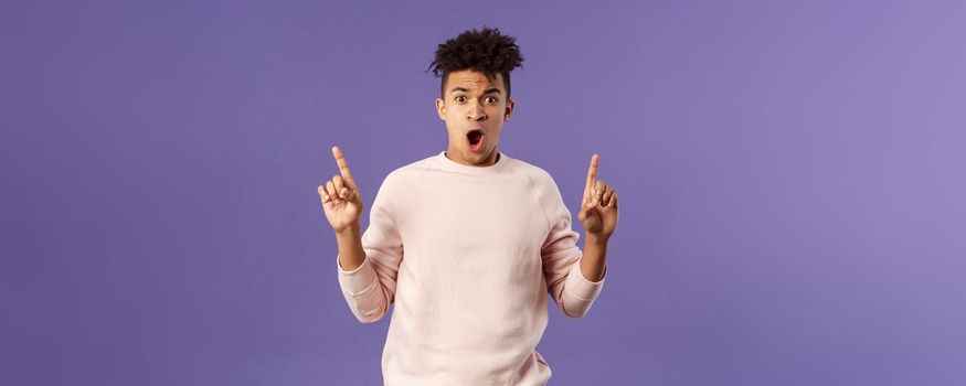 Portrait of shocked, speechless young hispanic man with dreads reacting to overwhelming shook news, gasping, drop jaw and staring concerned as pointing up at something astounding.