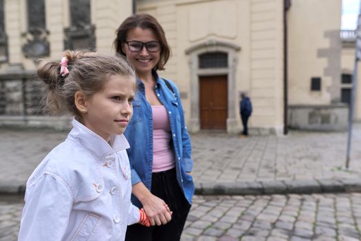 Mother and daughter child 8, 9 years old walking together along street of old city holding hands