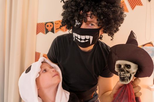 The concept of a homely cozy, Halloween family holiday. Happy dad and son are dressed in carnival costumes, holding a toy skeleton in their hands. family smiling and laughing