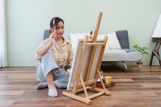 Joyful young female artist painting on canvas at workshop.