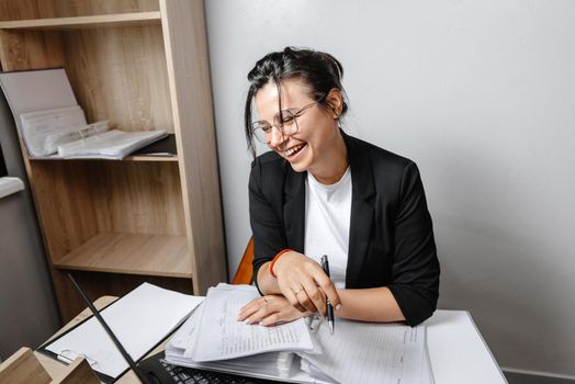 A smiling woman sitting at her desk in the office. A happy businesswoman sitting in her office. Worker in the office in a good mood