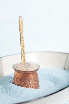 copper coffee pot with hot coffee on blue sand and blue background, beautiful blue color, coffee break, turkish coffee. High quality photo