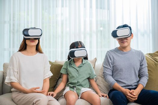 Happy family have mother father and daughter watching movie or playing video game, Asian family wear vr glasses headsets fun sitting on sofa in living room, game entertainment innovation technology
