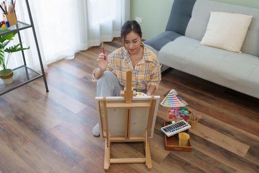 Joyful young female artist painting on canvas at workshop.