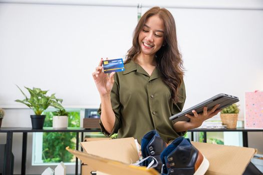 Asian young woman received online shopping parcel opening shoes boxes to checking on tablet, Cheerful woman holding credit card, happy female unpacking cardboard box, writing online store feedback