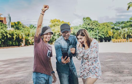 Three cheerful people looking at cell phone outdoors, Excited teenage friends looking at cell phone screen on the street. Three excited friends looking at the cell phone in the street