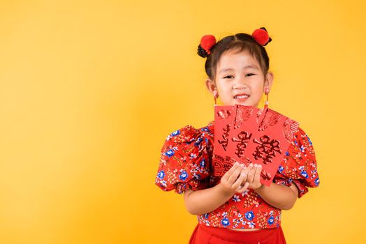 Chinese New Year. Happy Asian Chinese little girl smile wear red cheongsam qipao hold angpao red packet monetary gift, Portrait child in traditional dress, studio short isolated on yellow background