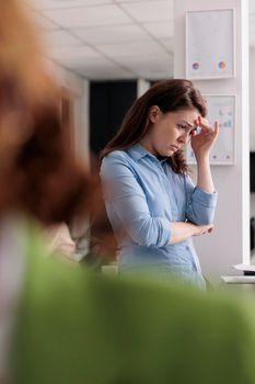 Depressed employee having professional burnout, suffering from headache at work, touching forehead, exhausted woman in coworking space. Frustrated person with migraine feeling unwell at workplace