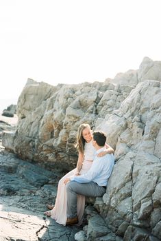 Smiling woman sitting on man lap on rocks. High quality photo