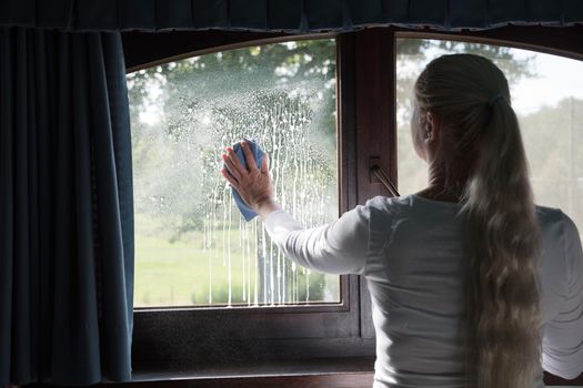 Woman cleaning window with special glass cleaner. Look through soapy window. High quality photo
