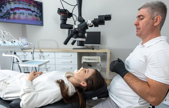 Dentist using dental microscope treating patient teeth at dental clinic office. Medicine, dentistry and health care concept