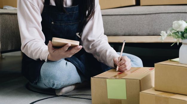 Startup Entrepreneurship Small Business SME Freelance Young lady working at home with boxes on the floor and laptop online Marketing Packaging SME