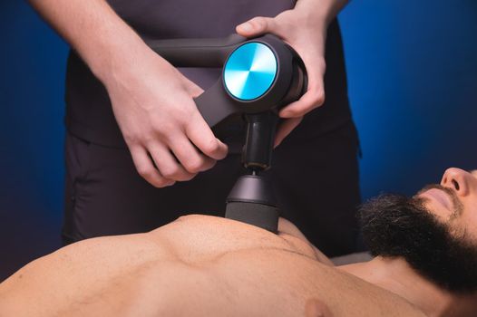 Close-up Sports percussion massage in the medical office of the gym. The masseur makes massage exercises. Percussion therapy for regenerating sports body massage. Sports injury rehabilitation concepts