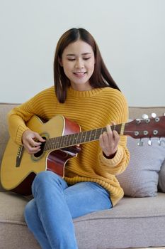Portrait of a woman playing guitar on the sofa happily in the house.