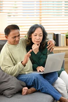 Happy retried couple enjoying spending time together at home and using laptop. Retirement and happy senior lifestyle concept.