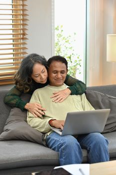 Happy retried couple enjoying spending time together at home and using laptop. Retirement and happy senior lifestyle concept.