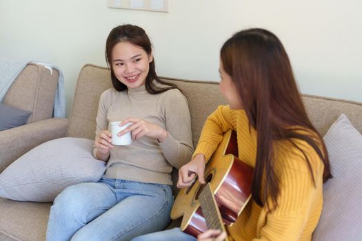 LGBTQ concepts, female couple playing guitar happily on the sofa in the house.