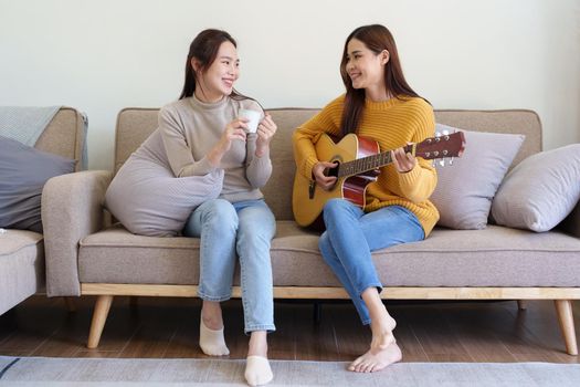 LGBTQ concepts, female couple playing guitar happily on the sofa in the house.