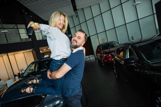 Happy caucasian couple hugging while buying a new car in a car dealership