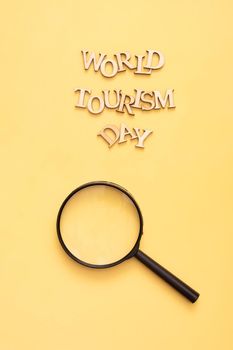 World Tourism Day text from wooden letters on a yellow background with a magnifying glass.