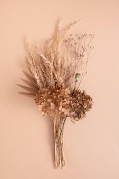 Bouquet of beige dried flowers, grass and leaves on beige background top view.