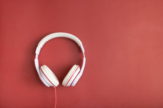 White-colored headphones on red background. Minimalistic fashion music concept. Copy space. Top view, flat lay.