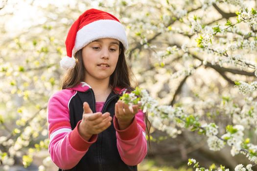 Little girl in santa hat playing in garden.