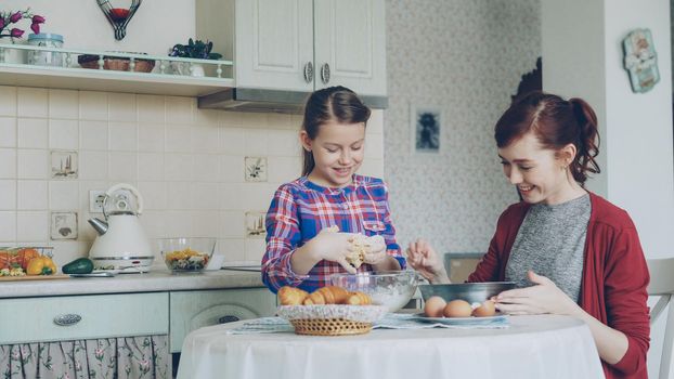 Little cute girl helping her mother in the kitchen stirring dough for cookies into bowl. Family, food, home and people concept