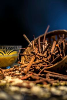 Close up shot of a bunch of manjistha herb roots in a container on a blue surface along with some other ingredients with it.