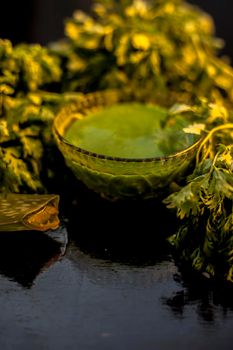 Anti-aging face mask on the black colored glossy surface consisting of fresh green Cilantro leaves, and some aloe vera gel. Prepared face mask with raw coriander and aloe vera. Vertical shot.