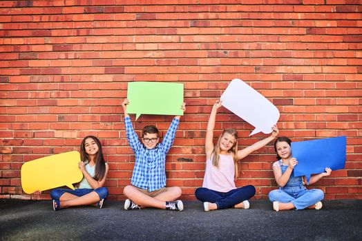 Please listen to what we have to say. Portrait of a group of young children holding speech bubbles against a brick wall