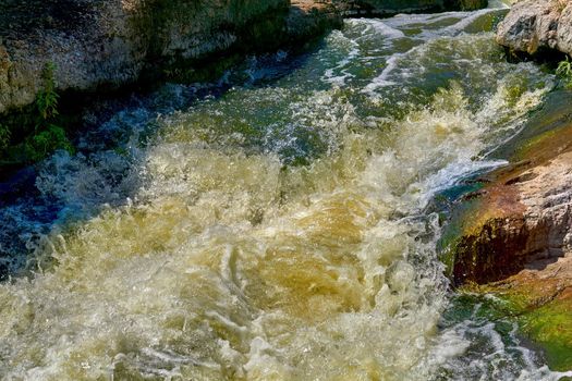 a large natural stream of water flowing in a channel to the sea, a lake, or another such stream. Stormy fast cleaner flow of a mountain river among a stone brown formation.