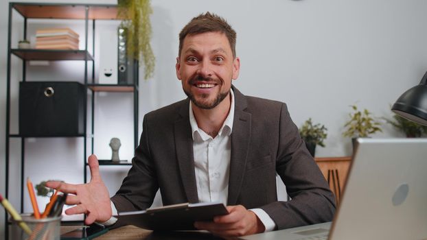 Oh my God, Wow. Businessman in suit working analysing paperwork documents raising hands in surprise, shocked by sudden victory, good news at home office desk. Confident male manager freelancer man