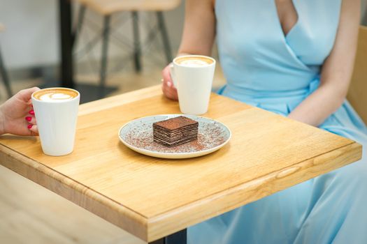 Two young women with cups of coffee and pieces of cake sitting at the table in a cafe outdoors