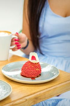 Young woman with cup of coffee and piece of cake sitting at the table in a cafe outdoors