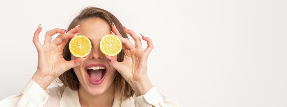 Portrait of a beautiful young woman with an open mouth holding two slices of orange at her eyes against a white background